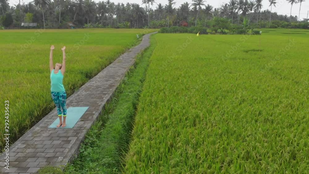 Aerial Slowmotion shot of a young woman practicing yoga on a beautiful rice field Aerial Slowmotion shot of a young woman practicing yoga on a beautiful rice field