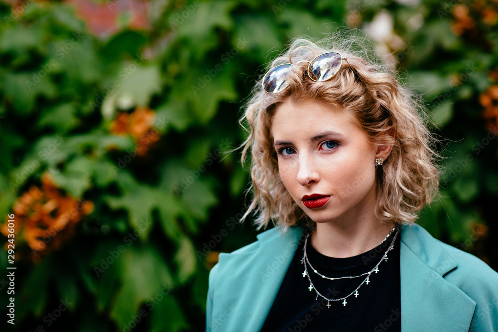 Portrait of a young curly haired blonde woman in front of greenery Portrait of a young curly haired blonde woman in front of greenery