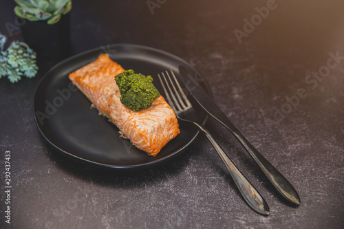 pink salmon fillet roasted grilled on a black plate with a scoop of pesto photo