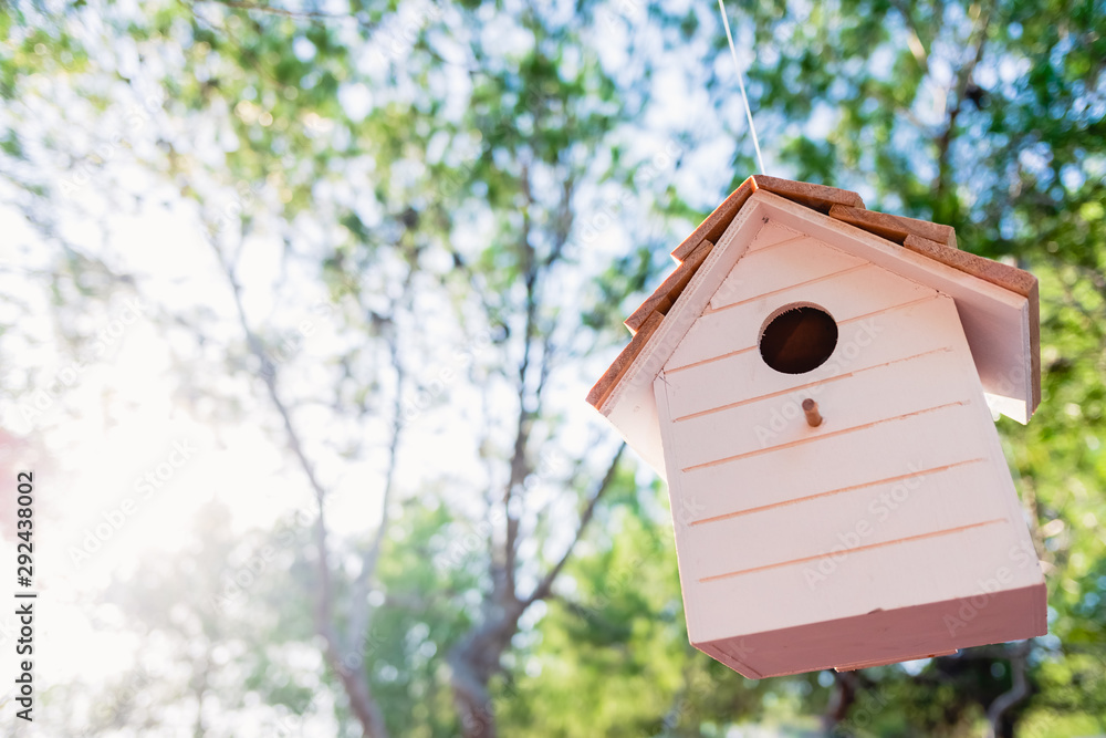 A wooden birdhouse with a background of unfocused trees and sun rays. A wooden birdhouse with a background of unfocused trees and sun rays.