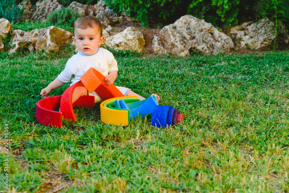 Baby playing with a colorful wooden rainbow on the grass, children's intellectual and mental development. Baby playing with a colorful wooden rainbow on the grass, children's intellectual and mental development.