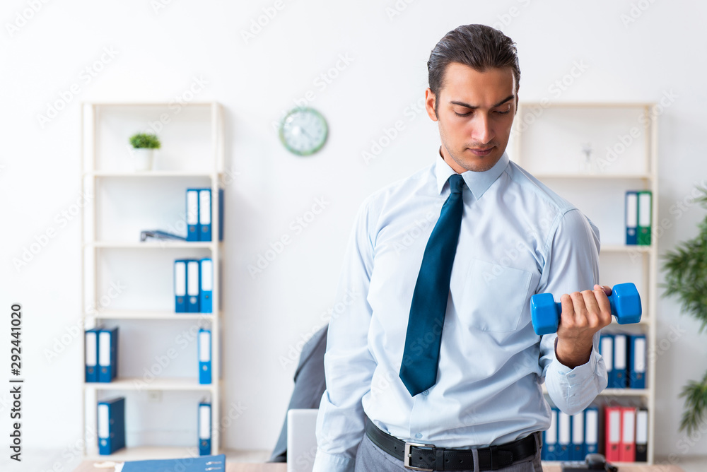 Young handsome employee doing sport exercises at workplace Young handsome employee doing sport exercises at workplace