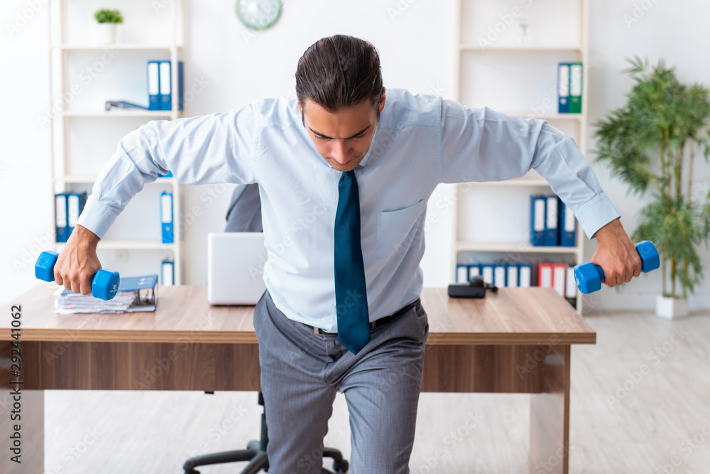 Young handsome employee doing sport exercises at workplace Young handsome employee doing sport exercises at workplace