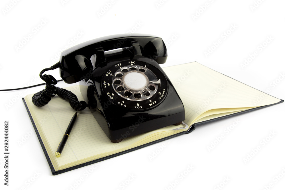 old black office telephone resting on a note book isolated on a white background