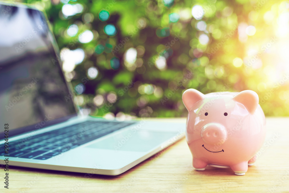 Piggy Bank with laptop on wood table in the public park.money saving financial concept. Piggy Bank with laptop on wood table in the public park.money saving financial concept.