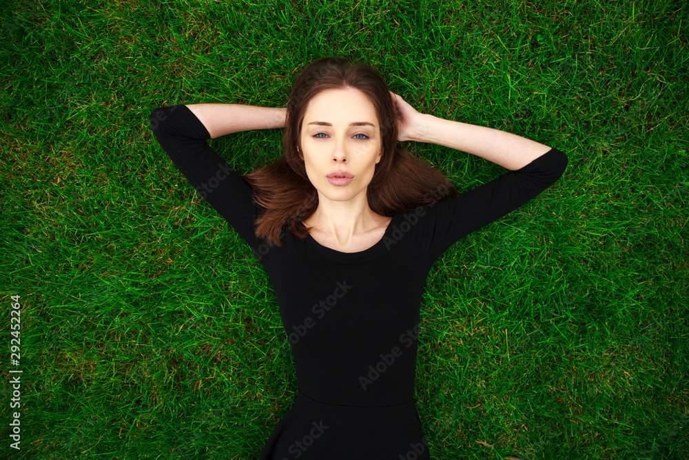 Top view portrait of a young beautiful woman in black dress lies on green lawn in a park Top view portrait of a young beautiful woman in black dress lies on green lawn in a park