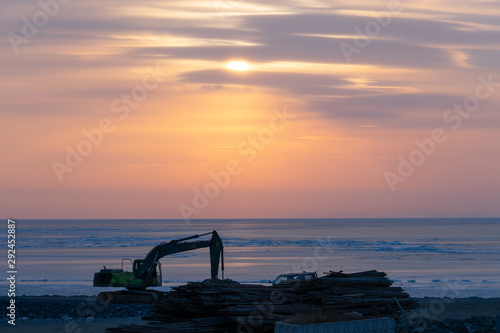 Excavator on the shore of the frozen sea against the sunset. © vvicca