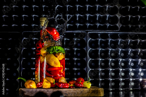 Peppers in motion ,colorful composition of peppers, chili sauce and preserved preserves in bottle and pot.