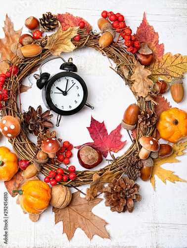 autumn background. harvest season. Black retro alarm clock, acorns, pumpkin, leaves, berries, nuts and cones on white table. autumn holiday, fall time concept. close up. 