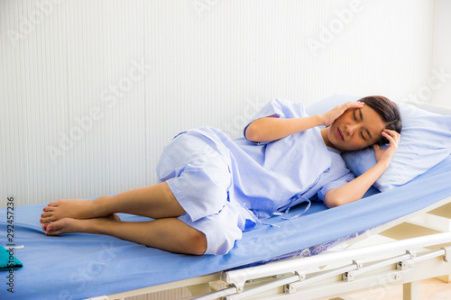 Asian young beautiful woman in the patient's dress lay on the patient bed in the hospital.The hand touched her head because of a headache.