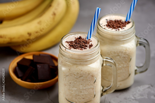 Banana milkshake in a glass with chocolate on grey concrete surface, closeup