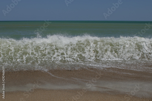 Sea wave floating on the sandy shore with foam and spray.