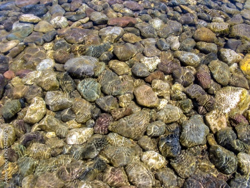 Clear water of river under sunlight. River stones in the clear river water. Background of river colored stones under water. Top view.