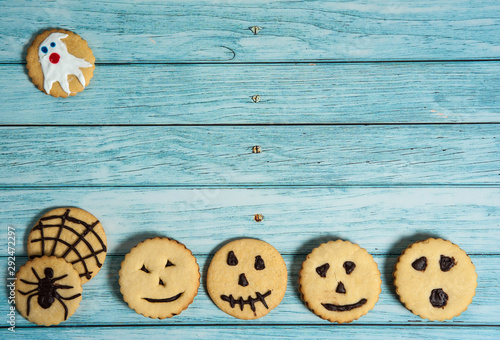 Homemade cakes for Halloween. Delicious cookies with horrible emoticons, cobwebs, spiders, ghosts on a light blue wooden background.
