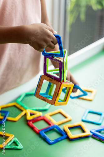 Girl in pink dress playing with magnetic geometric shape toy, hands show, no face.