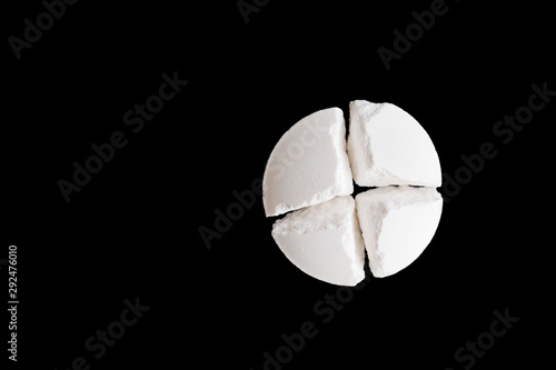 White pill broken into four parts on black background. Tablet cut twice. Top view. Copy space photo