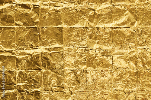 Golden color folded into squares and crumpled foil background. Wrinkled light gold metallic texture. Closeup