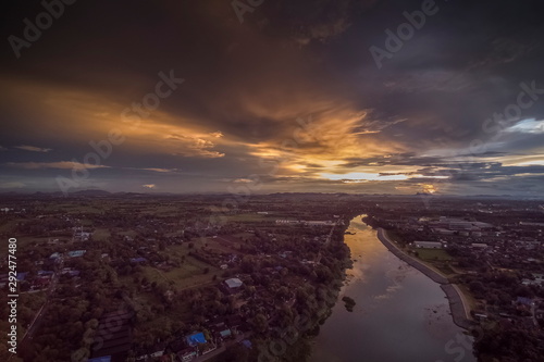 Aerial view evening above Mae Klong River around with green forest, village, building with cloudy sky background, sunset with raining in Ban Pong District, Ratchaburi, Thailand. © Yuttana Joe
