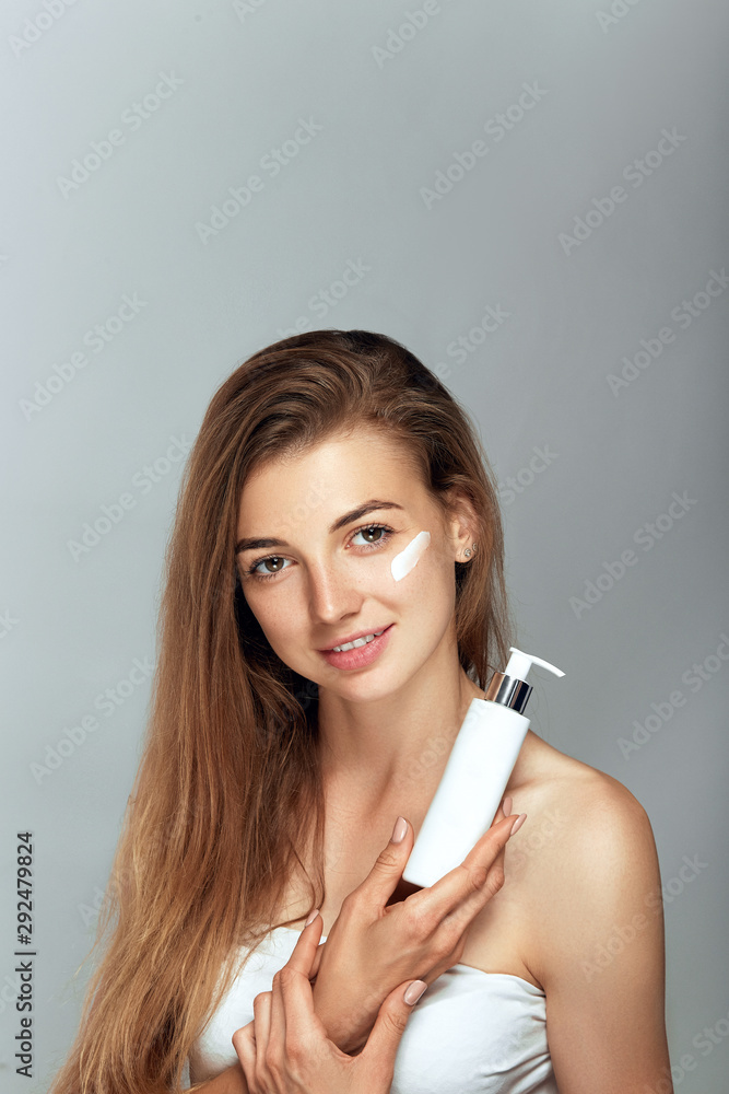 Beauty Woman Face Skin Care. Portrait Of Attractive Young Female Applying Cream And Holding Bottle. Closeup Of Smiling Girl With Natural Makeup And Fresh Skin. Beauty Cosmetics. Beauty Woman Face Skin Care. Portrait Of Attractive Young Female Applying Cream And Holding Bottle. Closeup Of Smiling Girl With Natural Makeup And Fresh Skin. Beauty Cosmetics.