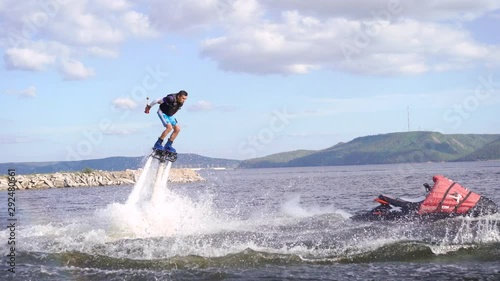 man is flying on flyboard on lake or sea in day, hydrocycle is floating near, water flows is lifting human photo