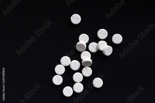 White round tablet pills placed at random on black background. Some of them have chipped edges. Top view. Flat lay. Copy space