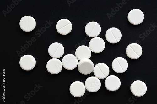 Fototapeta Naklejka Na Ścianę i Meble -  White round tablet pills placed at random on black background. Top view. Flat lay