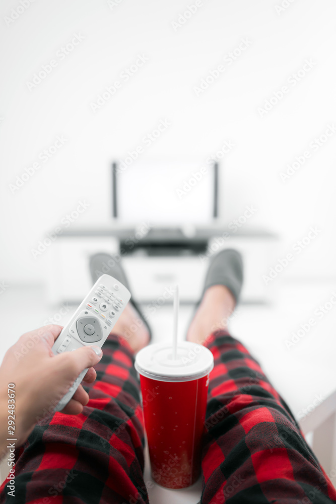 Man drinking soda juice and looking at TV with legs on the table in living room.