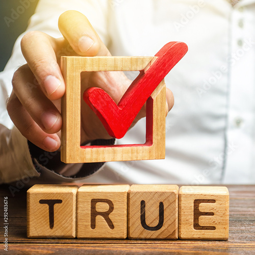 A man holds a red check mark over word True. Confirm the veracity and truth. Fight against fake news hostile propaganda. Confirmation facts, refutation of rumors. Debunking Myths and Misconceptions photo