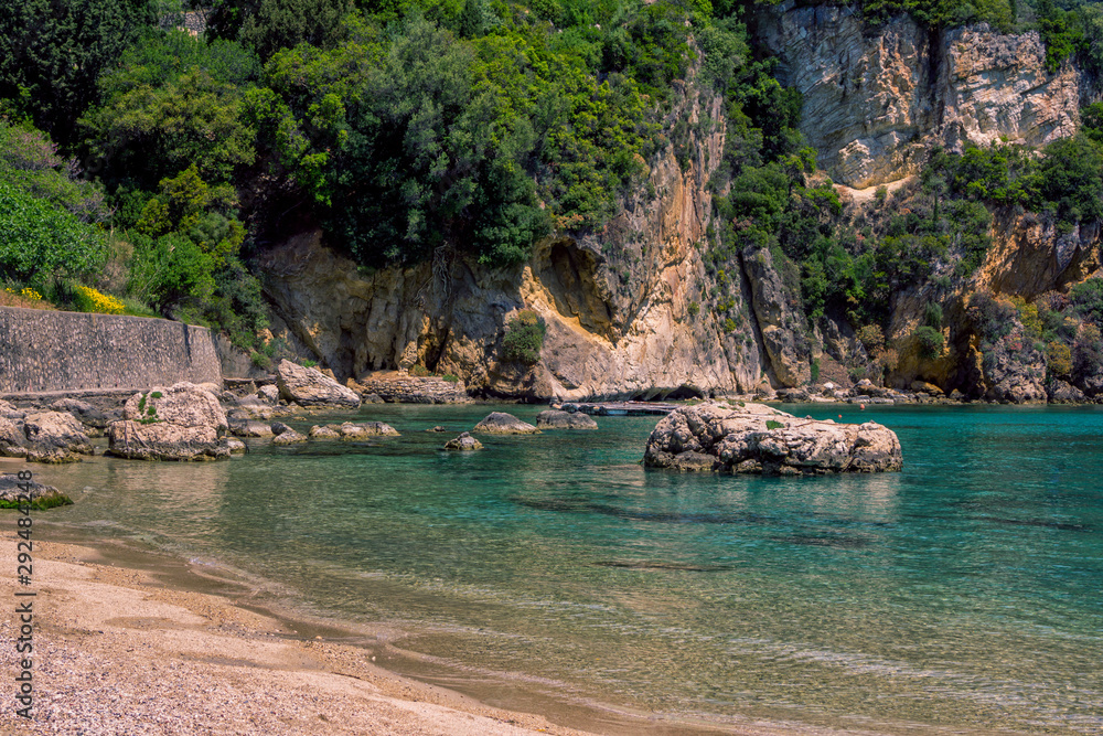 Seascape – lagoon with turquoise water, mountain with cliffs, green trees, bushes, rocks in a blue water. Corfu Island, Greece. 
