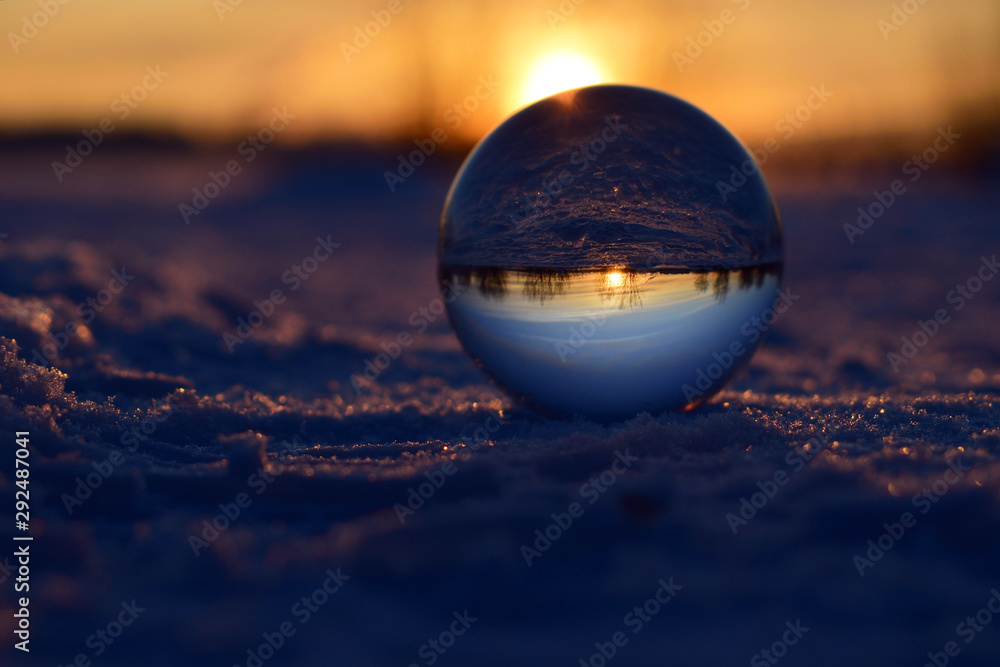 Glass sphere with reflection of sunset standing on snow surface. Purple colors. Winter nature background Glass sphere with reflection of sunset standing on snow surface. Purple colors. Winter nature background