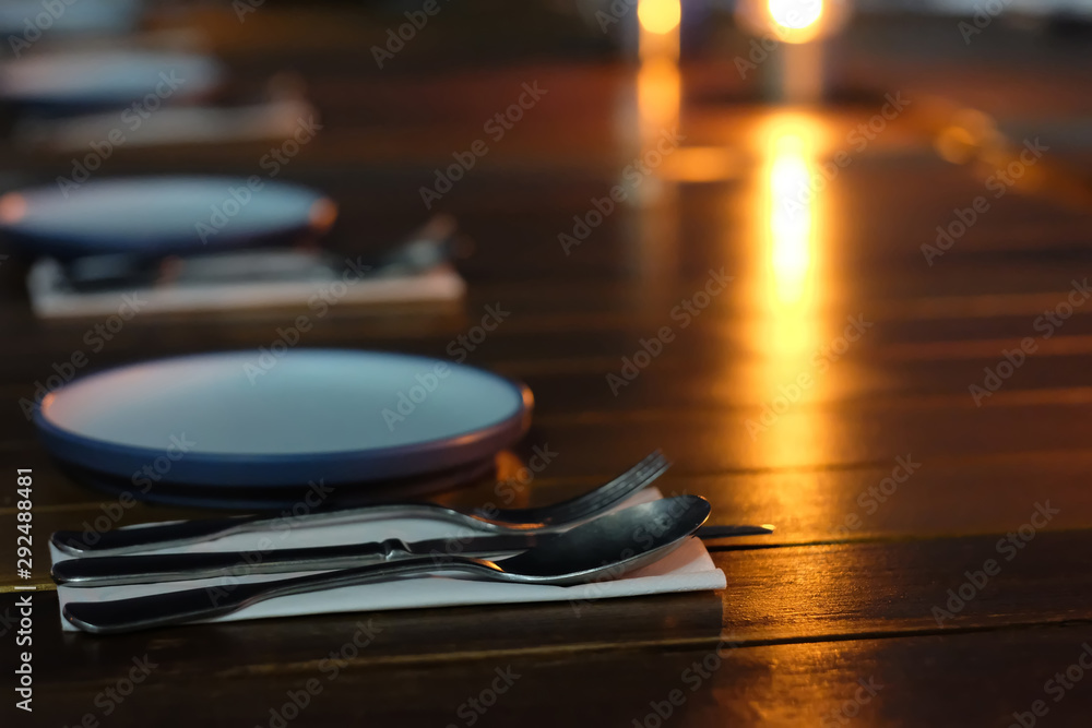Obraz premium close up plates and cutlery in a row on restaurant table at night. Shiny yellow light reflection on table
