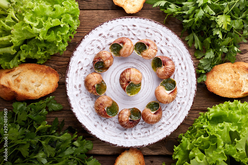 Escargots de Bourgogne - Snails with herbs butter on wooden background. Salad. Parsley.