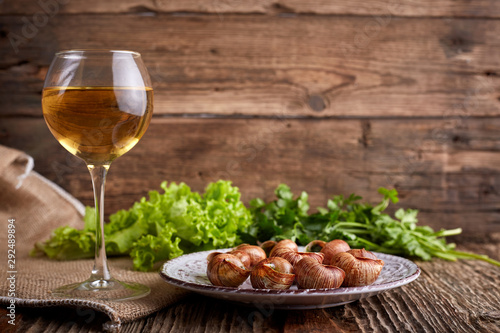 Escargots de Bourgogne - Snails with herbs butter on wooden background. Salad. Parsley. Glass of wine.