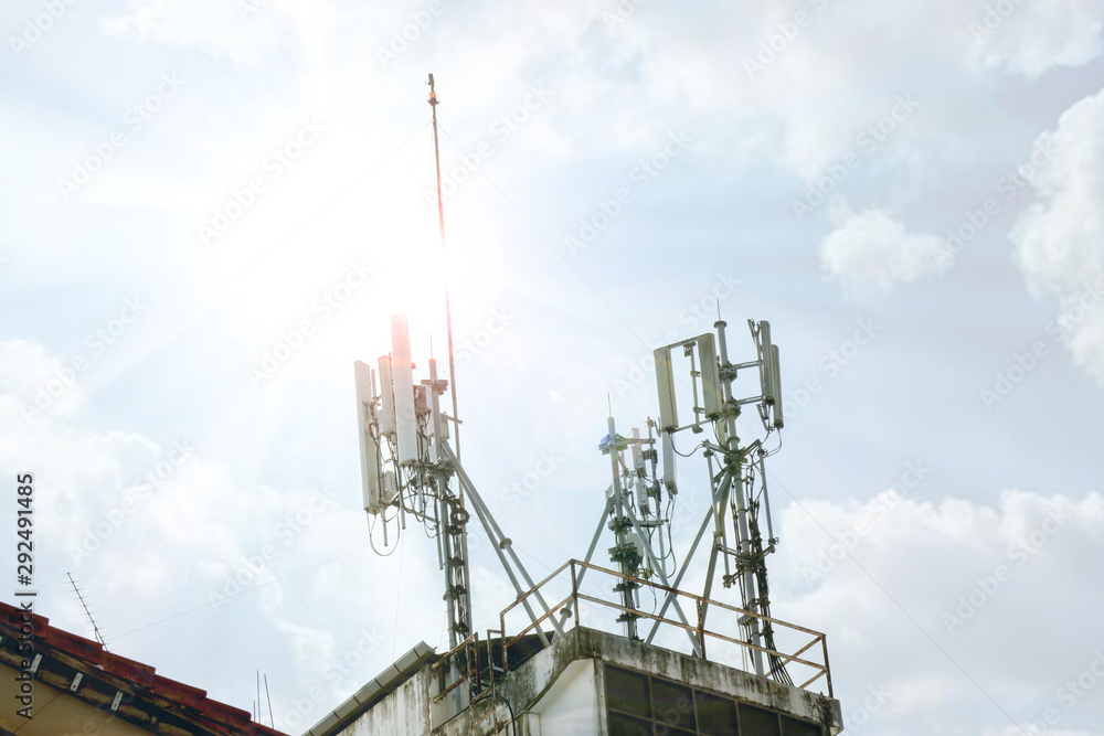Obraz premium Communication tower with antennas on the top of building on bright blue sky with cloud background.