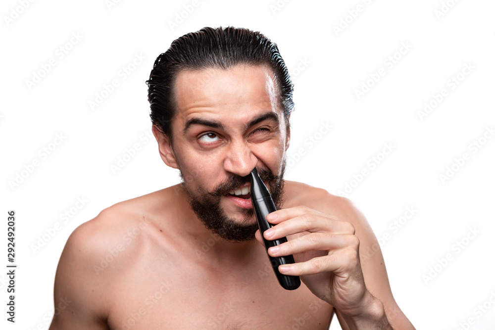 Handsome bearded man with mustache uses power trimmer to trim hair in the nose standning bare isolated over white background. Concept of morning treatment and shaving. Handsome bearded man with mustache uses power trimmer to trim hair in the nose standning bare isolated over white background. Concept of morning treatment and shaving.