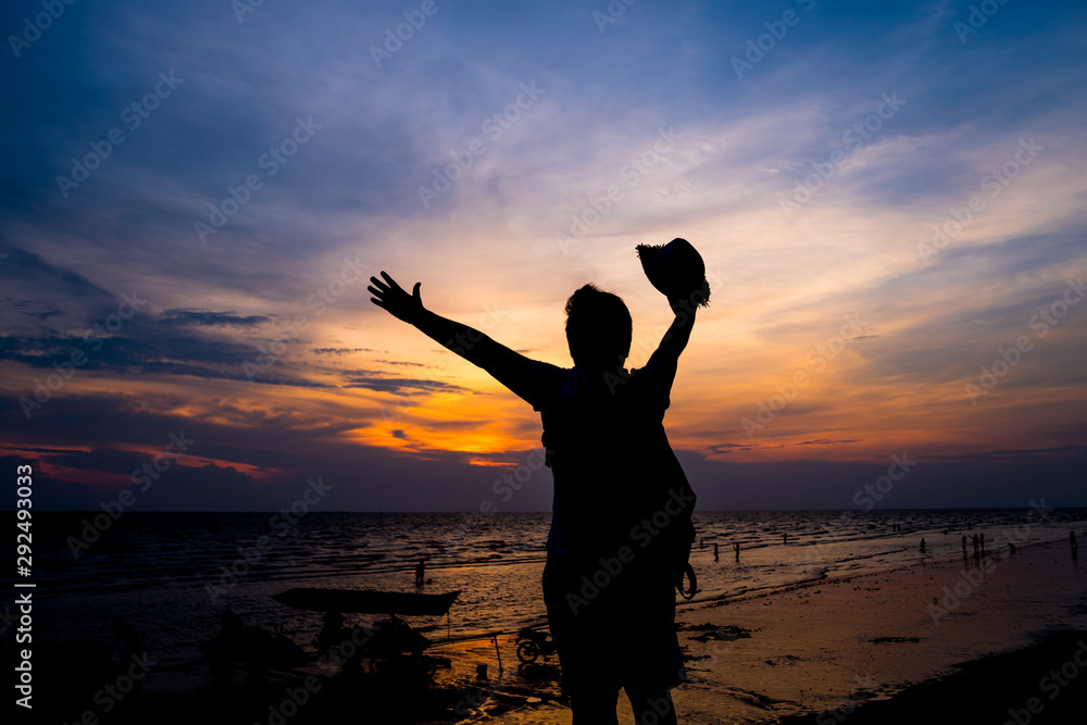 Traveler backpacker of freedom style Concept: Silhouette of Asian Young woman relaxing standing on rock seabeach, Strong confidence open her arms and watching sunset scene in summer sunset sky outdoor