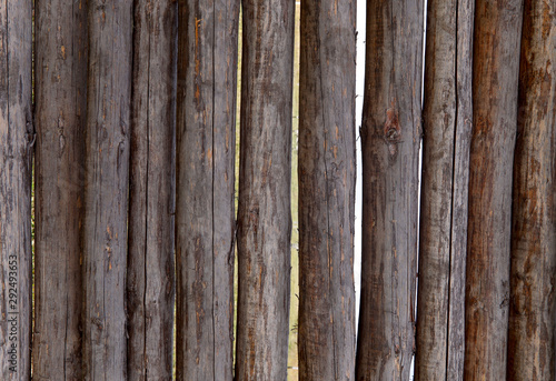 Background texture of a wooden fence of logs. Brown logs interconnected vertically. Cropped shot, horizontal, close-up. Concept of design and construction.