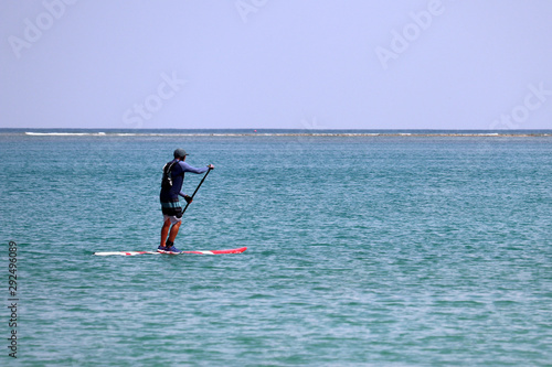 Man with paddle standing on a board in open sea, sup surfing. Surfer on a blue water, standup paddleboarding © Oleg