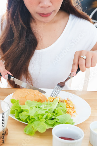 Eating breakfast omelette, bread, hamburger and vegetables on a white plate using a knife and fork