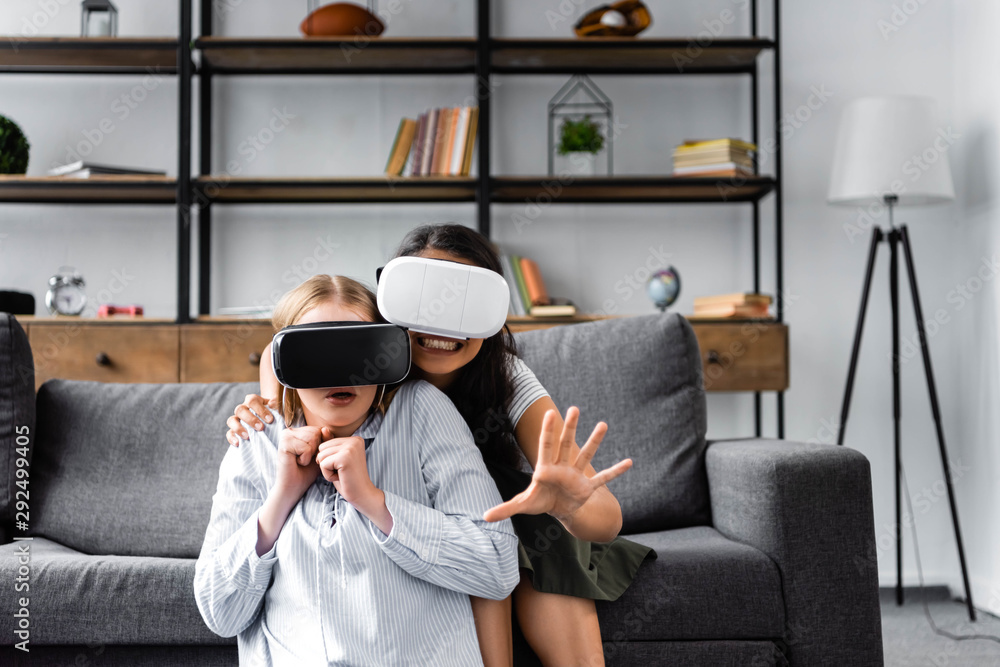 Obraz premium smiling multicultural friends with virtual reality headsets in apartment