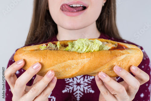 Unhealthy eating concept. Cropped closeup photo of cheerful excited nice crazy tongue-out fast food eater holding huge sandwich in hands isolated grey background