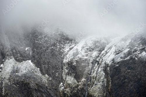 Stunning dramatic landscape image of snowcapped Glyders mountain range in Snowdonia during Winter with menacing low clouds hanging at the peaks photo