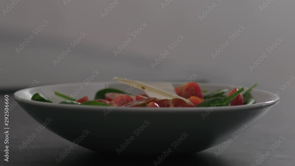 Slow motion cheese slices falling into bowl with cherry tomatoes and spinach leaves on kitchen countertop Slow motion cheese slices falling into bowl with cherry tomatoes and spinach leaves on kitchen countertop