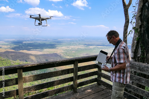 Photographer controls his drone from a viewpoint into wide landscape, drone against blue sky with white clouds, Chapada dos Guimarães, Mato Grosso, Brazil, South America photo