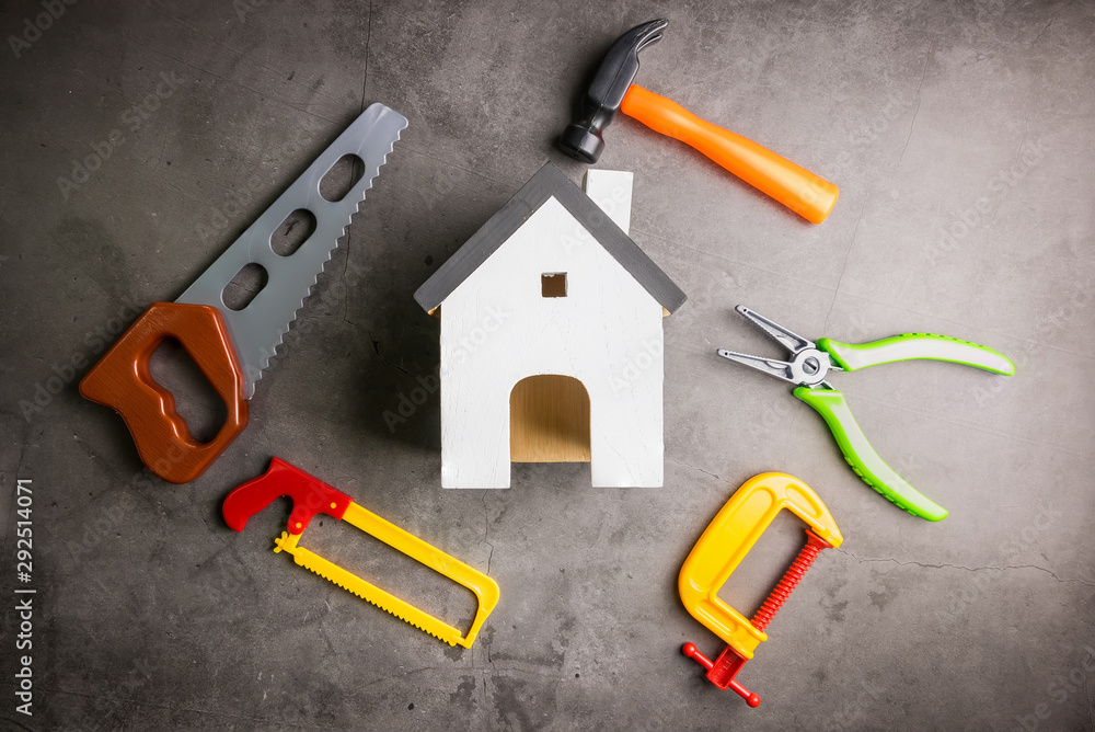 Wooden house and construction tools toy on stone pattern background with copy space.Home Repair concept, Repair maintenance concept, Renovation concept. Wooden house and construction tools toy on stone pattern background with copy space.Home Repair concept, Repair maintenance concept, Renovation concept.
