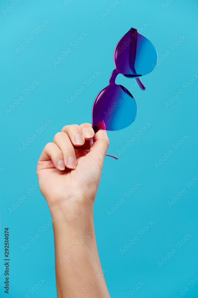 Image of hand with sunglasses on empty blue background Stock Photo