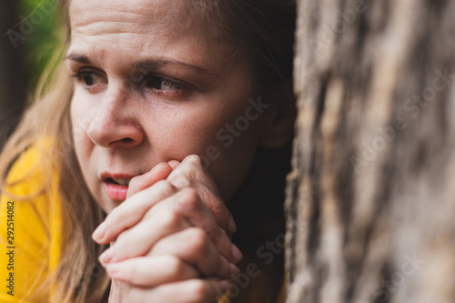 Φωτογραφία Close-up shot of a woman with paranoia hiding behind a tree