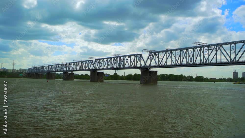 Time Lapse: Metallic railway bridge over Ob river against cloudy sky in city, boat sailing over flowing water - Novosibirsk, Russia Time Lapse: Metallic railway bridge over Ob river against cloudy sky in city, boat sailing over flowing water - Novosibirsk, Russia