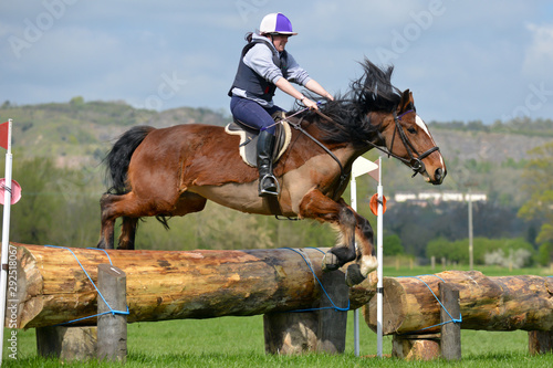 Up and over, young woman and her horse jumping over a large log jump in the English countryside. a