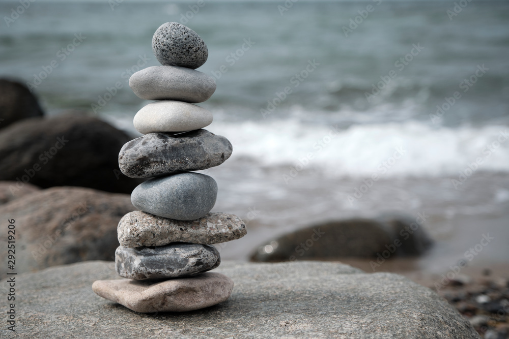 Ein aus acht flachen Steinen aufgebauter Turm, der auf einem am Strand liegenden Felsstein aufgesetzt wurde mit im Hintergrund verschwommen aufgenommen Welle der Ostsee Ein aus acht flachen Steinen aufgebauter Turm, der auf einem am Strand liegenden Felsstein aufgesetzt wurde mit im Hintergrund verschwommen aufgenommen Welle der Ostsee